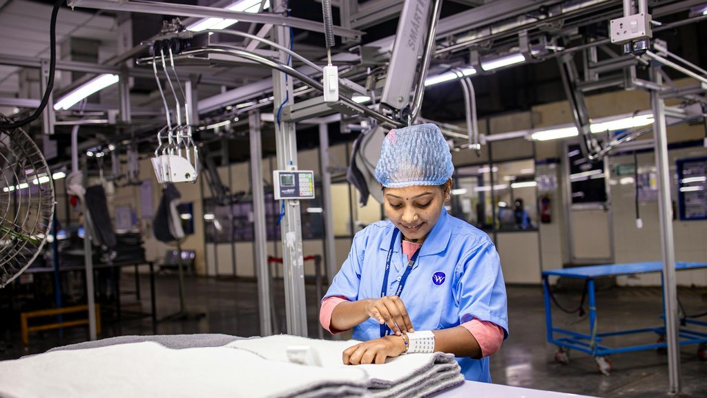 Aufnahme von EqualStock IN aus einer Textilfabrik zeigt eine Frau in blauer Uniform, die gefaltete Kleidungsstücke auf einem Tisch sortiert.